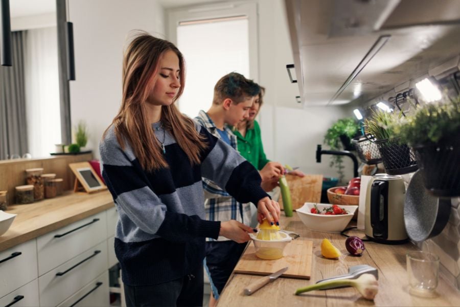 Ungdomar och familjehemsmamma lagar mat tillsammans i köket