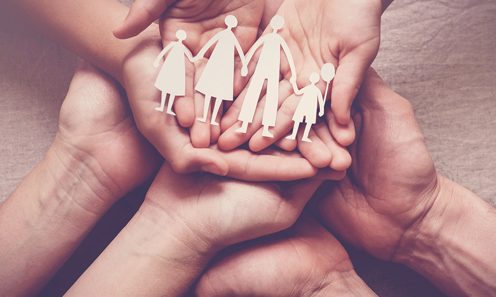 Händer som håller pappersdockor som representerar en familj, symboliserar stöd och gemenskap