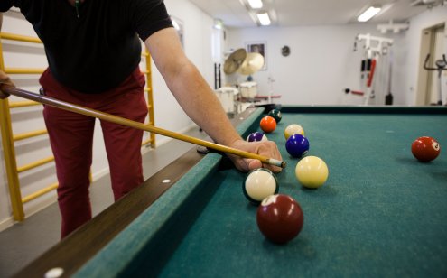 Person spelar biljard i ett gym, fokuserar på att stöta en vit biljardboll på ett biljardbord