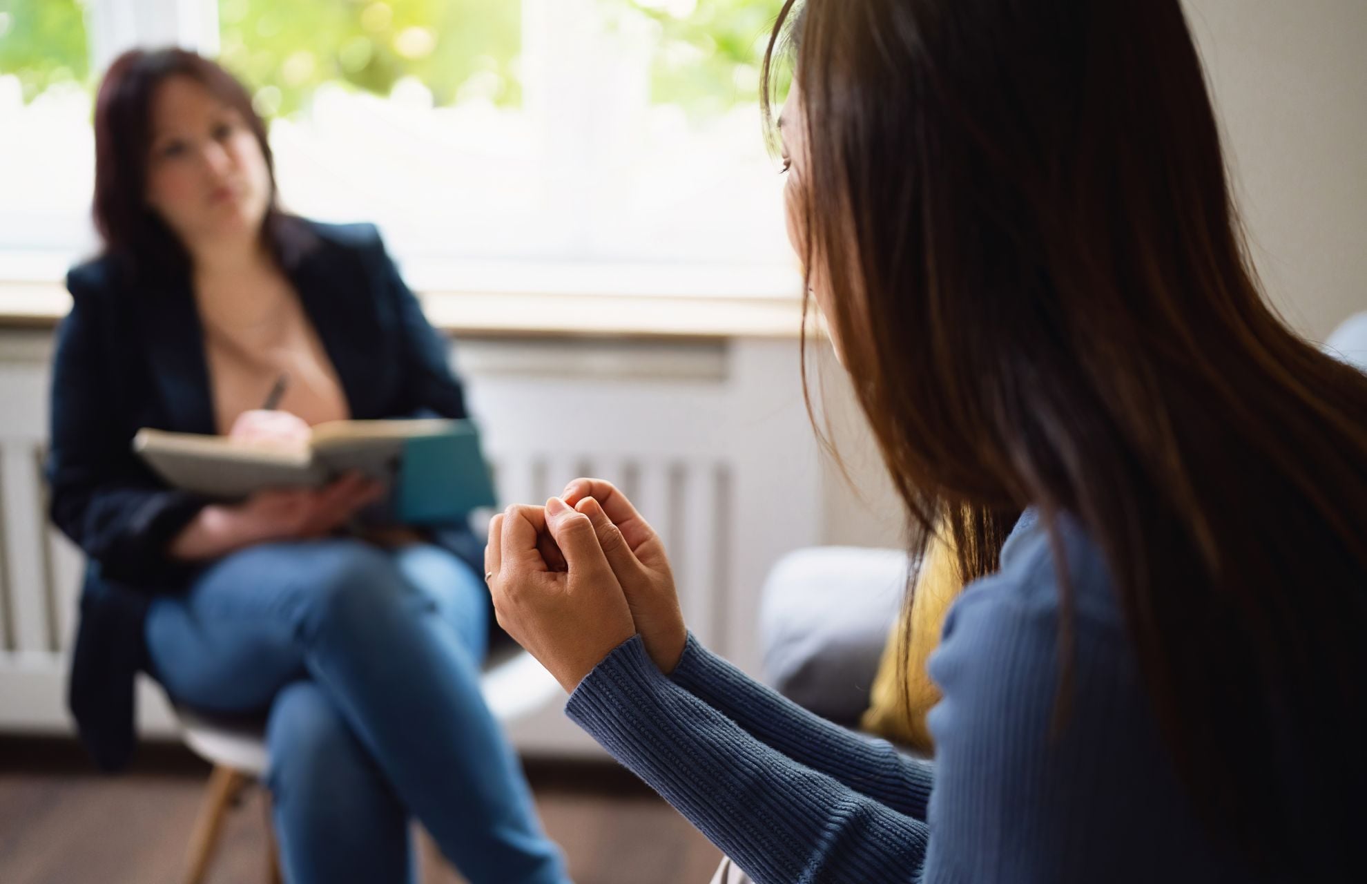 Ung kvinna samtalar med terapeut som antecknar i bok