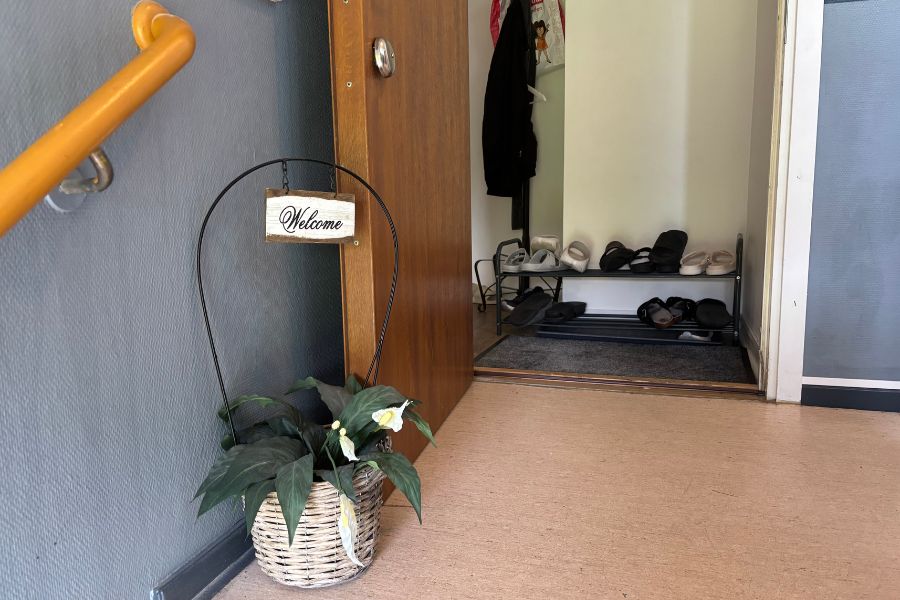 Blomma i trapphuset med skylt välkommen och öppen dörr in till hall