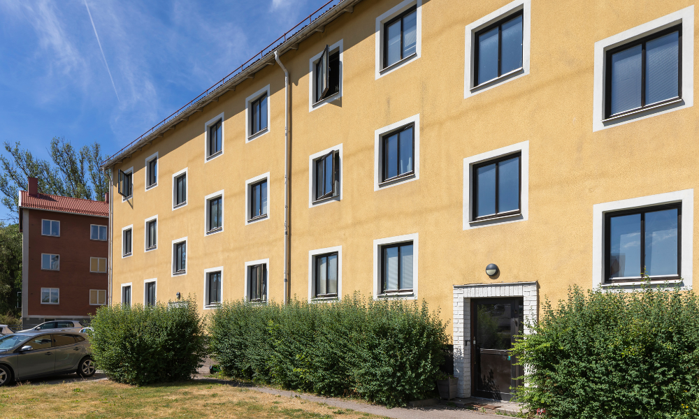 Gult flerfamiljshus omgiven av gröna buskar