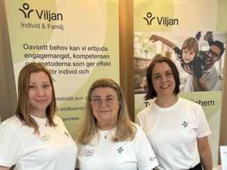 Tre kvinnor står framför en monter för Viljan Individ & Familj, klädda i vita tröjor med företagets logotyp